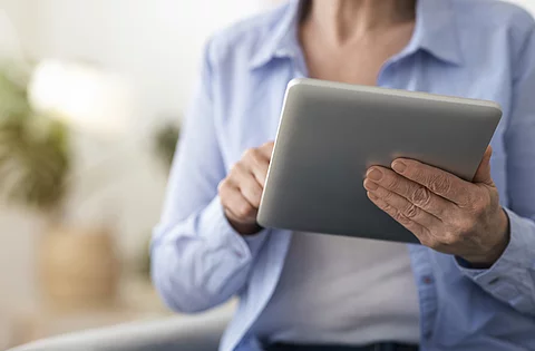 Digital Tablet In Hands Of Unrecognizable Senior Woman Sitting At Home