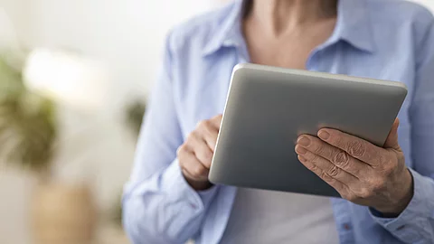 Digital Tablet In Hands Of Unrecognizable Senior Woman Sitting At Home