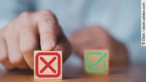 Hand schieben einen Holzwürfel mit rotem Kreuz nach vorne, ein Würfel mit grünem Haken bleibt im Hintergrund