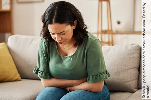 Stress, stomach pain and woman on a sofa with menstruation, gas or constipation, pms or nausea at home. Gut health, anxiety and lady with tummy ache in living room from ibs, bloated or endometriosis