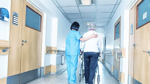 Asian doctor helping elder woman with walker in hospital hallway