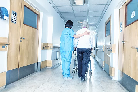 Asian doctor helping elder woman with walker in hospital hallway