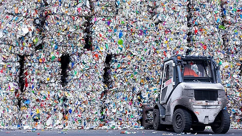 Ein kleines Arbeitsfahrzeug steht vor meterhohen, dicht gepressten Ballen aus buntem Plastikmüll auf einem Recyclingplatz