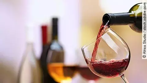 Weinflaschen und Weingläser auf einem Tisch; ein Weinglas wird aktuell befüllt..