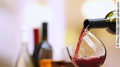 Weinflaschen und Weingläser auf einem Tisch; ein Weinglas wird aktuell befüllt.