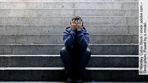 ein junger Mann sitzt auf einer Betontreppe und hält die Hände vor das Gesicht ein junger Mann sitzt auf einer Betontreppe und hält die Hände vor das Gesicht
