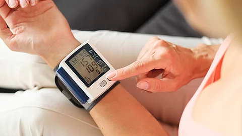 mit HypEine Person misst ihren Blutdruck mit einem elektronischen Handgelenk-Blutdruckmessgerät.ertonie Eine Person misst ihren Blutdruck mit einem elektronischen Handgelenk-Blutdruckmessgerät.