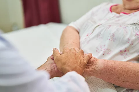 Ein Arzt hält die Hände eines Patienten – eine Geste der Nähe und des Trostes. Die Szene vermittelt Fürsorge und Empathie