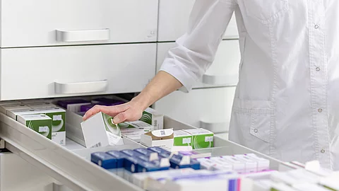 Eine Person in weißem Kittel sortiert Arzneimittelpackungen in einer Apothekenschublade.