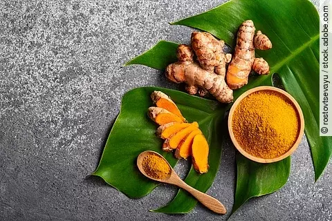 Turmeric powder and fresh turmeric root on grey concrete backgro