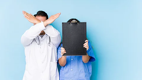 Young doctor couple posing in a blue background isolated keeping two arms crossed, denial concept.