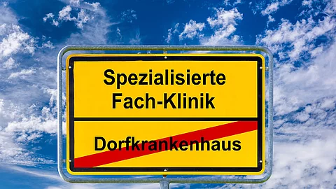 Ein Ortsschild ist beschriftet mit Dorfkrankenhaus und Spezialisierte Fach-Klinik - FOTOMONTAGE Ein Ortsschild ist beschriftet mit Dorfkrankenhaus und Spezialisierte Fach-Klinik - FOTOMONTAGE