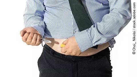 Eine Person injiziert sich ein GLP-1-Medikament in die Bauchregion. Die Aufnahme zeigt den Oberkörper in Hemd und Krawatte, während die Spritze angesetzt wird.