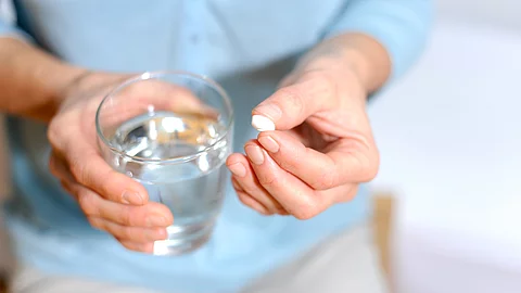 Frau hält eine Tablette und ein Glas Wasser in der Hand