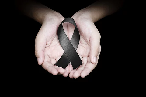 Hand holding black ribbon on black background mourning awareness