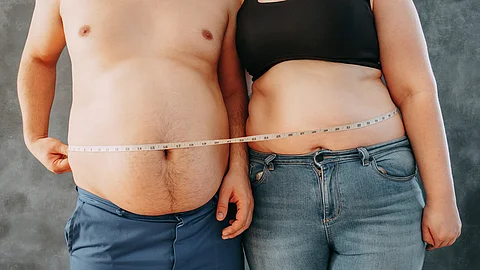 Ein übergewichtiges junges Paar steht eng zusammen und ist mit einem Maßband umwickelt.