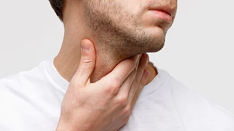 Close up of sick man suffering from throat problems, grey background, isolated. Thyroid gland, painful swallowing, pharyngitis, laryngeal swelling concept. Inflammation of the upper respiratory tract