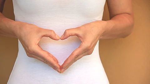 Frau macht ein Herz am Bauch mit ihren Händen