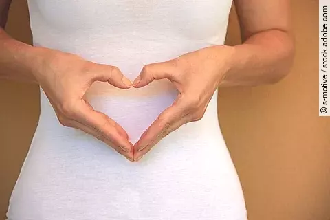 Frau macht ein Herz am Bauch mit ihren Händen