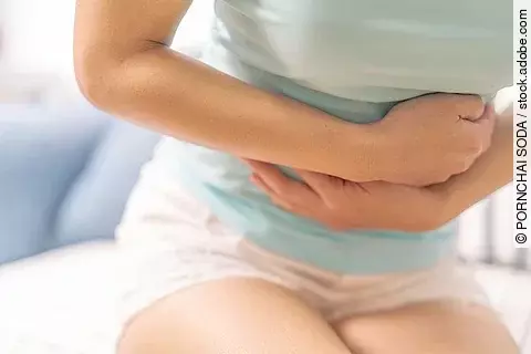 Young woman suffering from abdominal pain while sitting on the sofa and feeling stomachache, symptom of pms